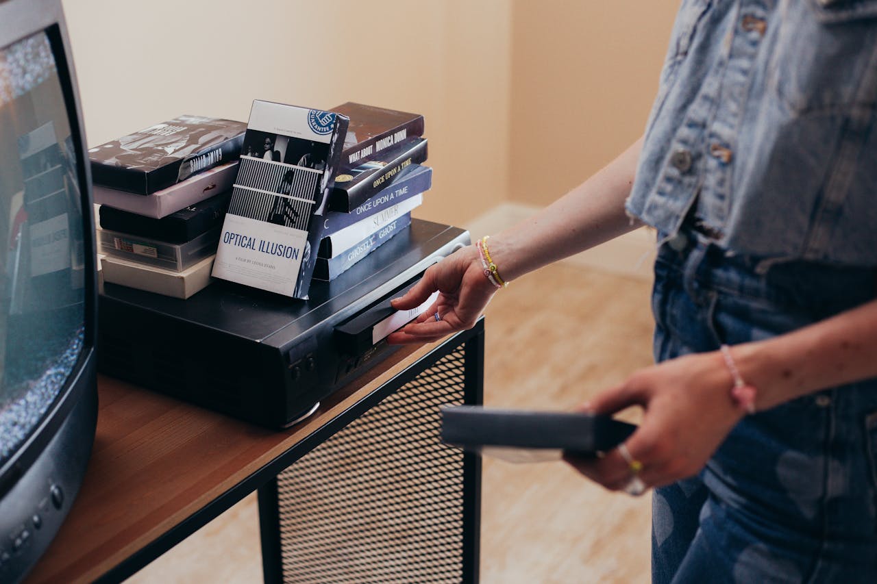 A person setting up a VCR with VHS tapes in a cozy indoor setting.